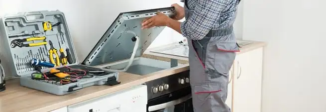 Cooktop repair technician lifting a built-in stovetop for service in Staten Island, NY