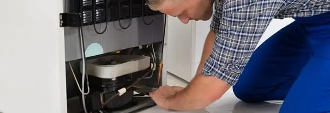 Refrigerator repair technician servicing the compressor and condenser area in Staten Island, NY