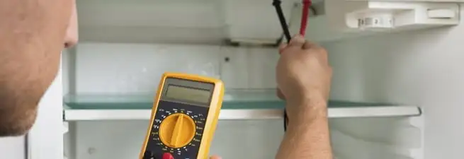 Refrigerator repair technician testing electrical components with a multimeter in Staten Island, NY