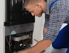 Refrigerator repair technician servicing the compressor and condenser area in Staten Island, NY